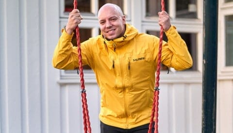 A bald man in a yellow jacket deftly swinging on a rope.