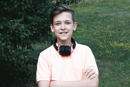 A young boy with headphones enjoying music in front of a tree.