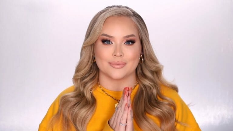 A woman in a yellow sweater is calmly praying in front of a white background.